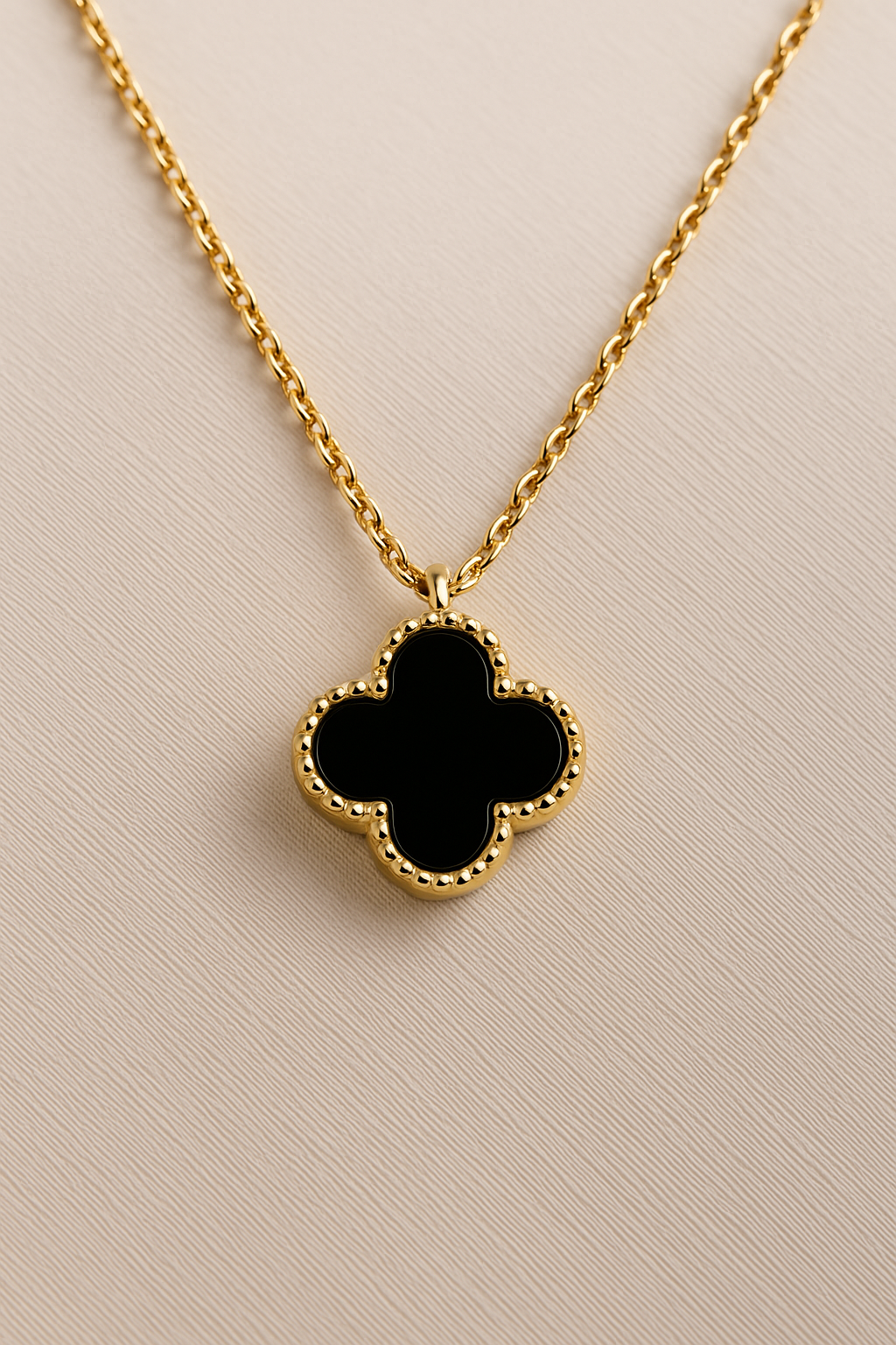 Gold-plated black clover pendant necklace displayed on jewelry stand.